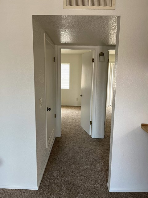 A hallway with white walls and carpeted floor.