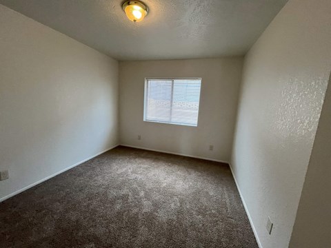 A room with a carpeted floor and a window with blinds.