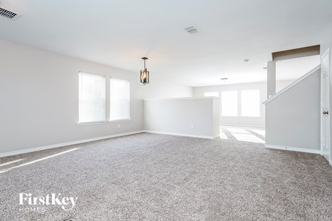 A spacious room with a carpeted floor and a staircase on the right side.