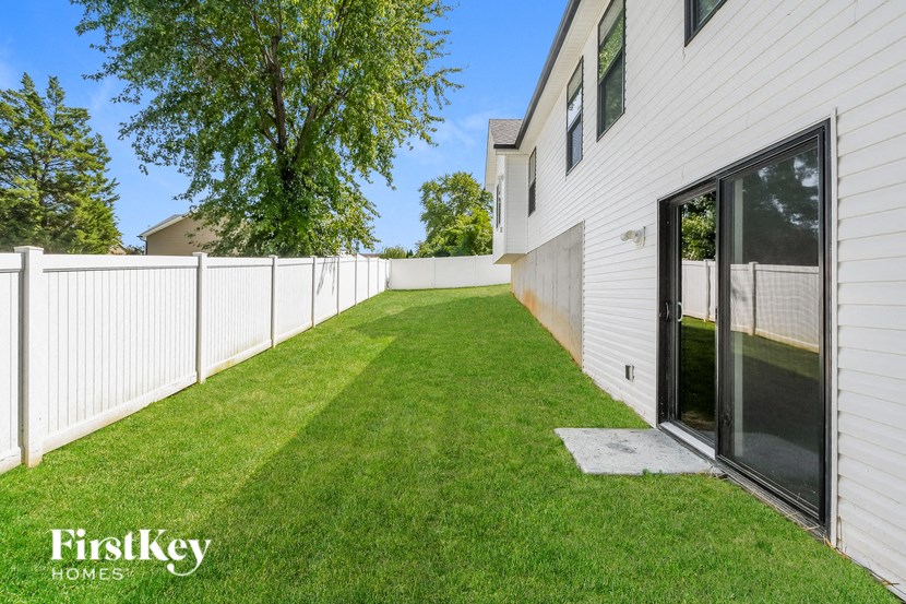 the backyard of a white house with a white fence and grass