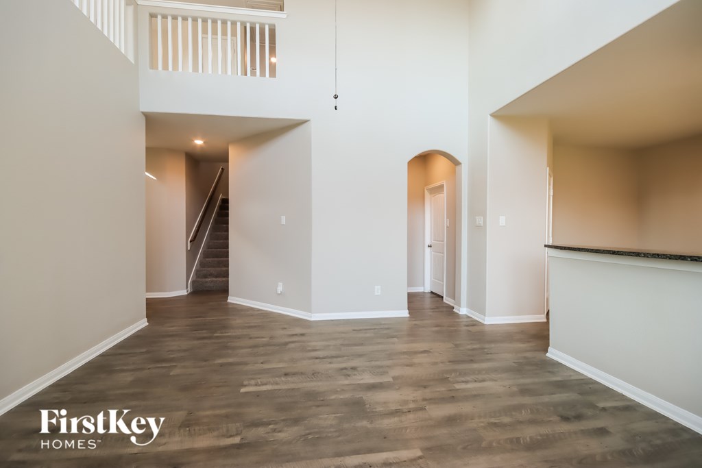 A spacious room with wooden flooring and a staircase in the background.