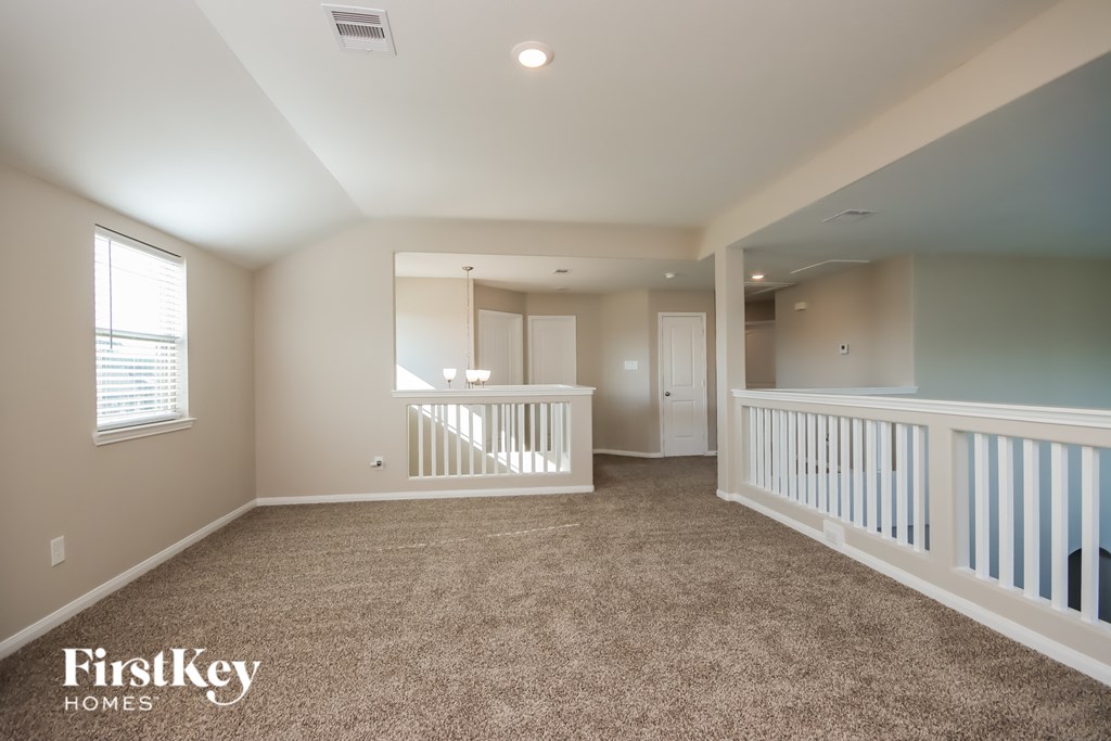 A spacious room with a carpeted floor and a staircase with white railings.