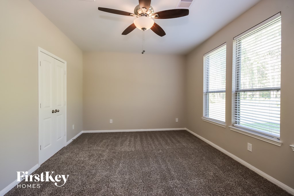 A room with a carpet floor, a ceiling fan, and a window with blinds.
