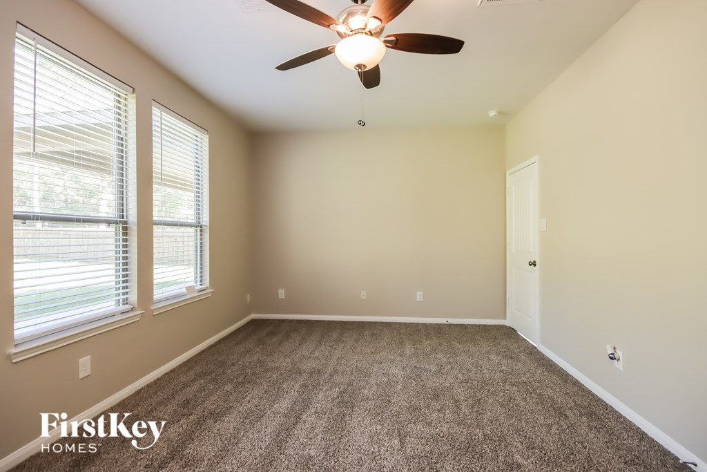 A room with a carpet floor, a ceiling fan, and a window with blinds.