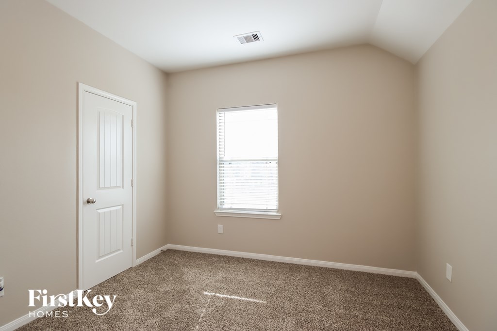 A room with a carpeted floor, a door, and a window with blinds.