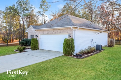 A white house with a garage is surrounded by a green lawn and trees.