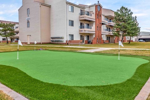 A green putting green in front of apartment buildings.