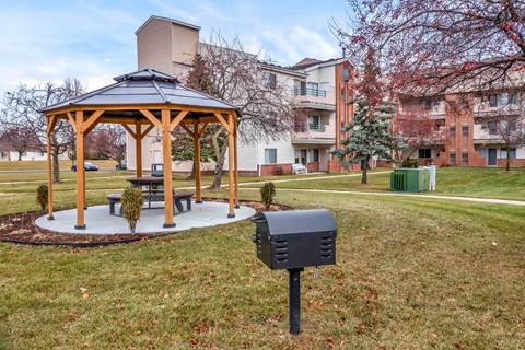 A gazebo with a picnic table sits in a grassy area in front of apartment buildings.