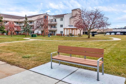 A wooden bench sits on a concrete slab in a grassy area.