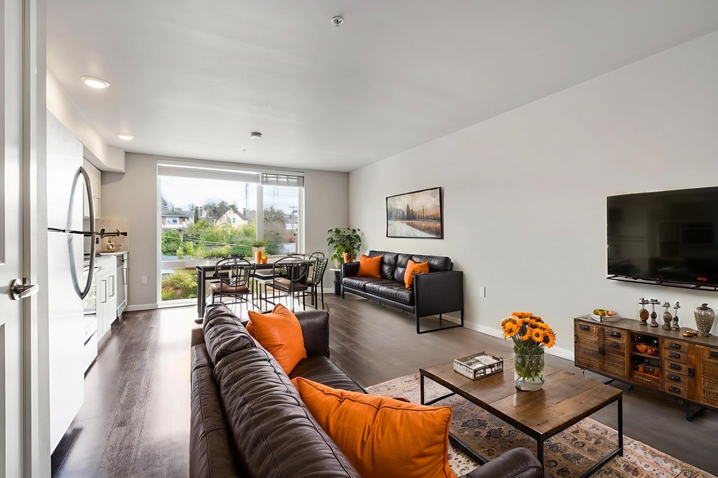 A modern living room with a black leather couch and orange pillows.