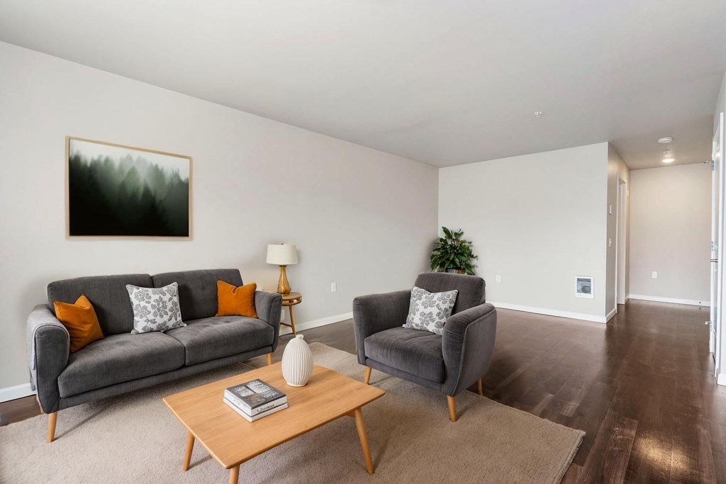 A living room with a grey couch, a grey armchair, a wooden coffee table, and a painting on the wall.