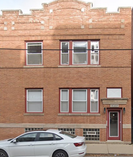 A white car is parked in front of a red brick building.