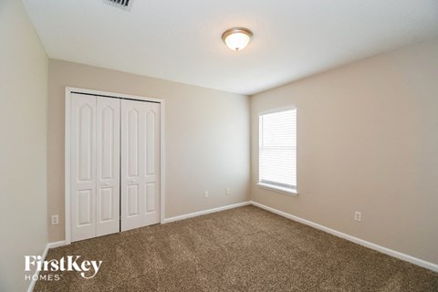 A room with a carpeted floor, a white door, and a window with blinds.