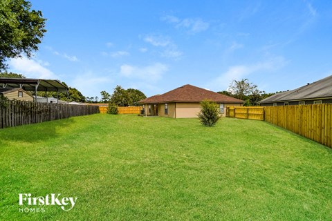 A grassy backyard with a house and a fence.