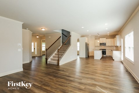 A spacious living room with wooden floors and a staircase leading to the upper level.