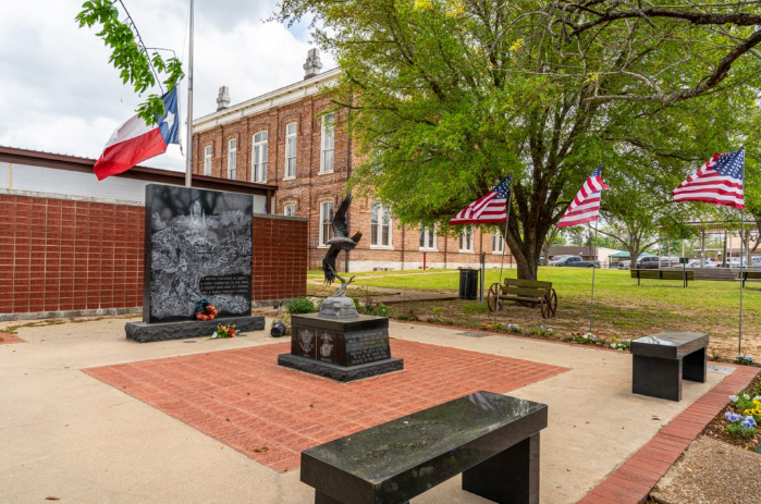 a courtyard with a statue and flags in front of a brick building