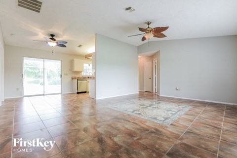 an empty living room with two ceiling fans and a kitchen