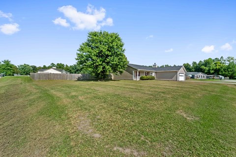 A large grassy field with a house and a tree in the distance.