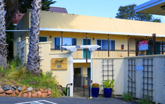 the front of a yellow motel building with a gate and a palm tree