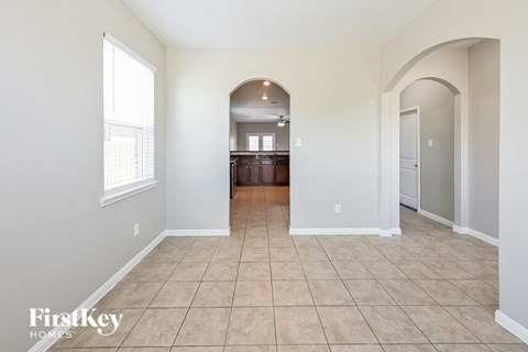 A spacious room with beige tiled flooring and a large arched doorway leading to another room.