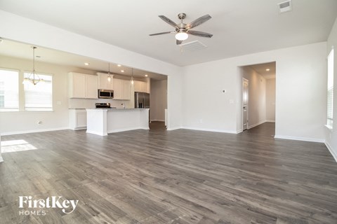 an empty living room with a kitchen and a ceiling fan