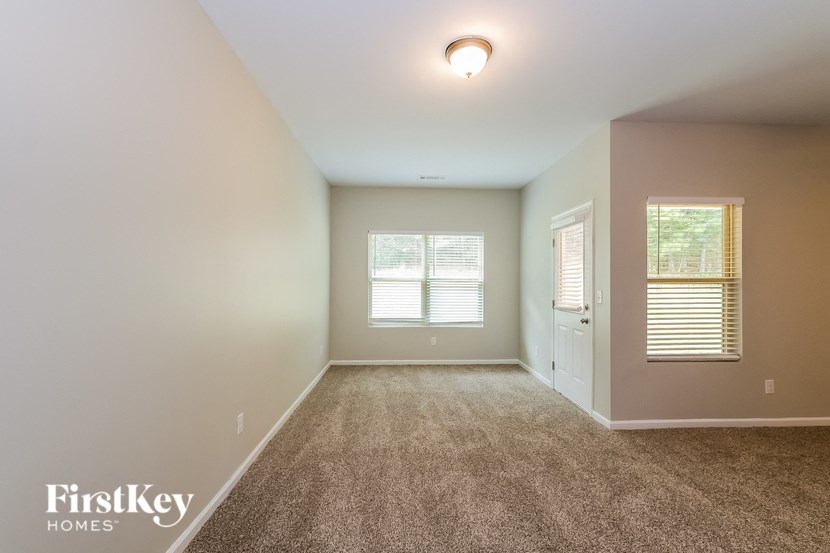 A spacious room with a carpeted floor and a window with blinds.