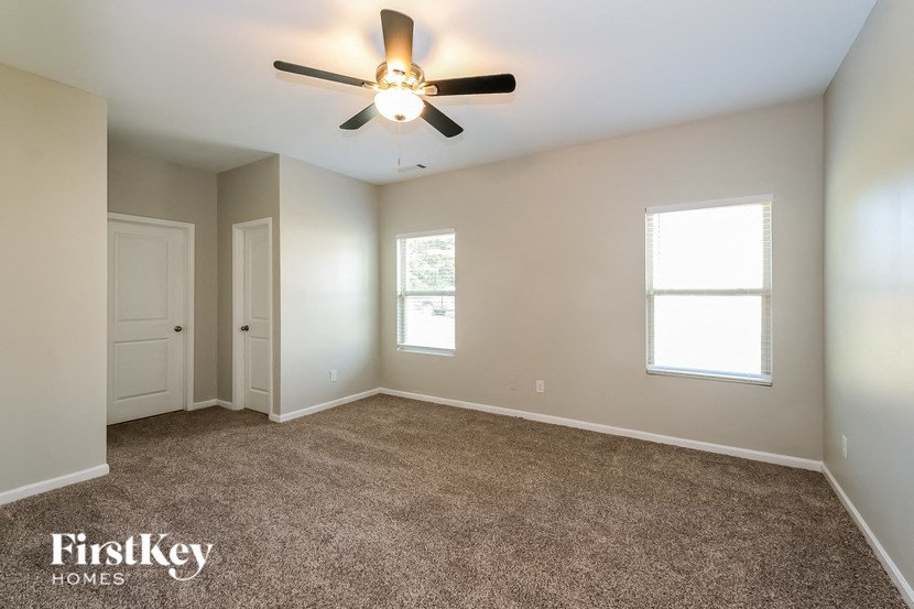 A spacious room with a ceiling fan and two windows.