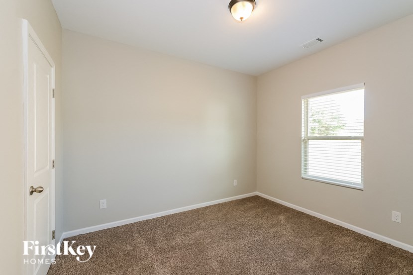 A room with a carpeted floor, a window with blinds, and a door.