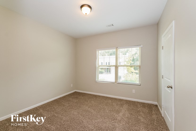 A room with a carpeted floor, a window with blinds, and a door.