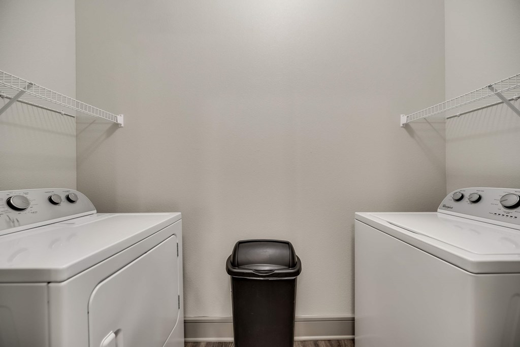 two washer and dryers in a laundry room with a trash can