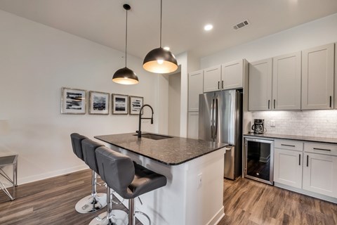 a kitchen with a large island with bar stools and a stainless steel refrigerator