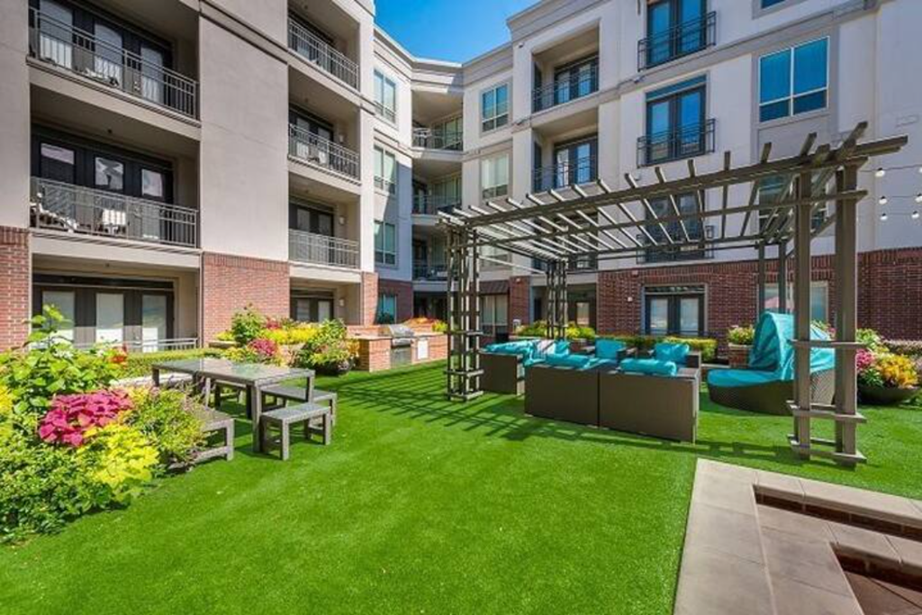 an apartment yard with green grass and furniture in front of an apartment building