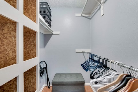 the closet in the laundry room is equipped with racks and a stool