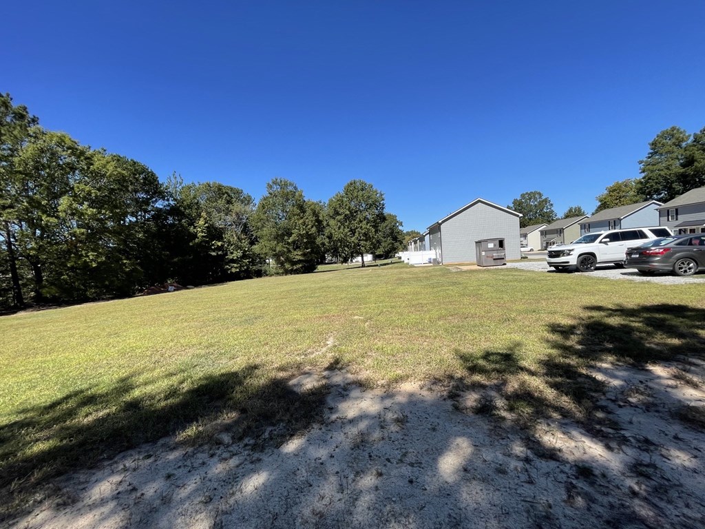 a grassy area with a house and cars in the background