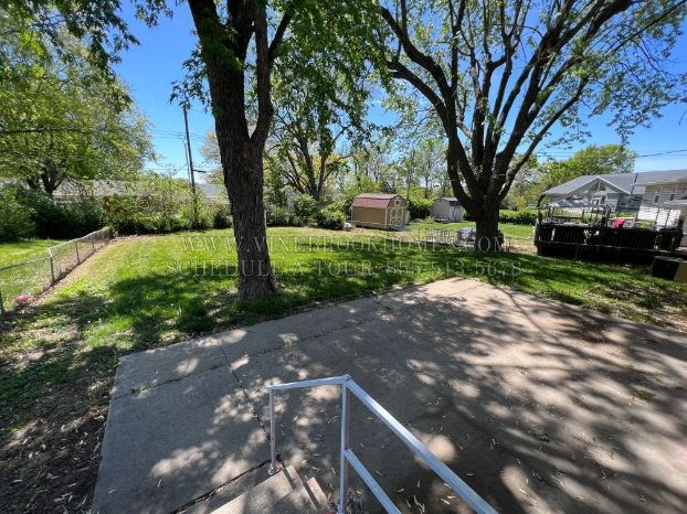 A tree-lined yard with a concrete walkway and a metal railing.