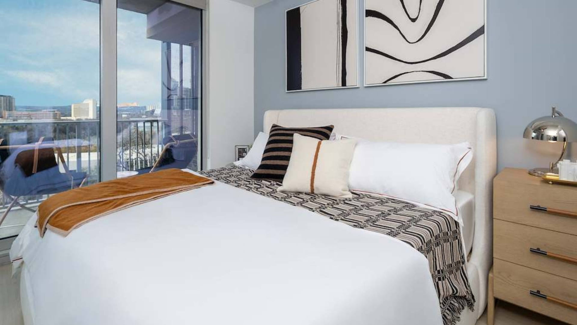 A bedroom with a large bed, a chair, and a window overlooking a cityscape.