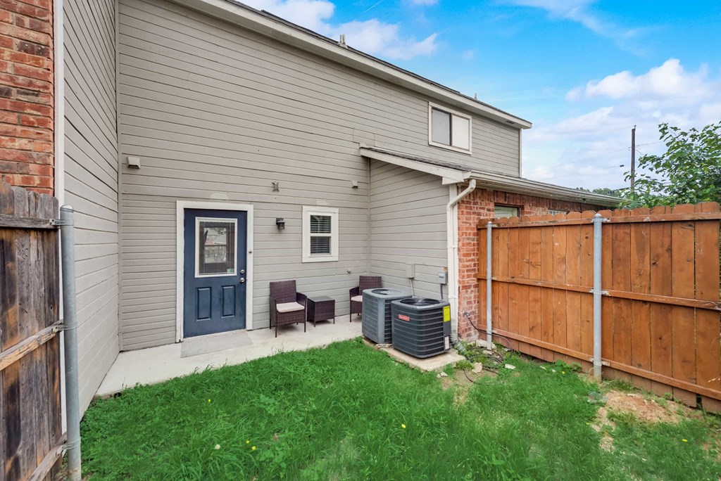 a backyard with a white house and a wooden fence and a patio with two chairs