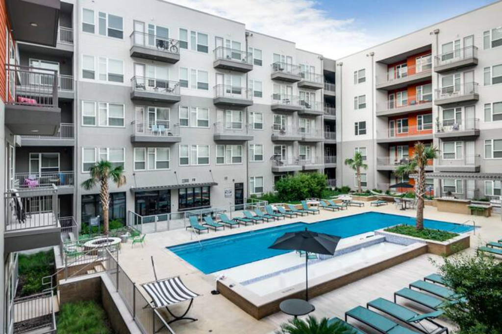 a pool with lounge chairs in front of an apartment building