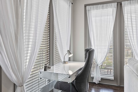 A white chair is in front of a desk with a lamp on it.