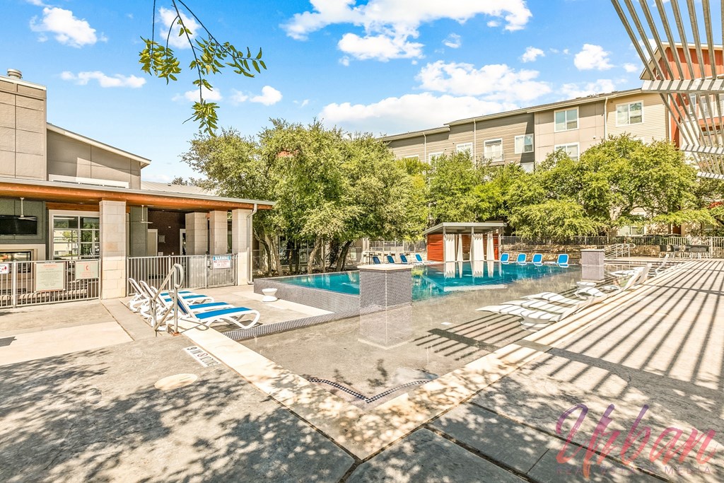 a swimming pool with lounge chairs and a building with trees