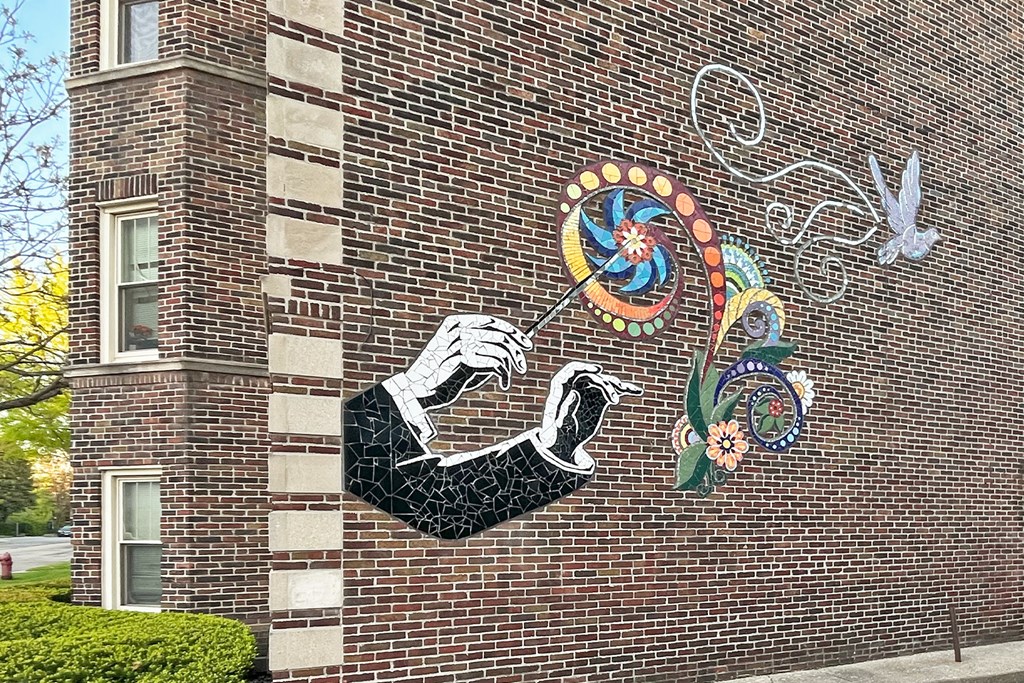 A mural on a brick wall depicts a hand holding a pen and a colorful design.