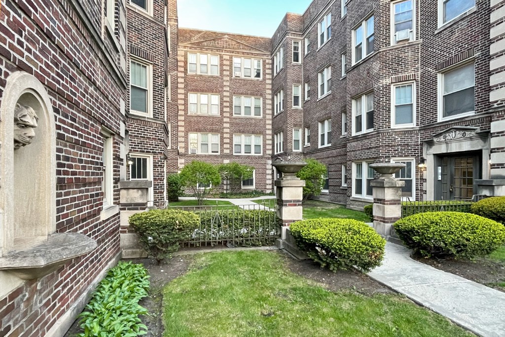 A courtyard surrounded by brick buildings with a statue on the left.