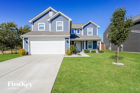 A blue house with a white garage door and a tree in front of it.