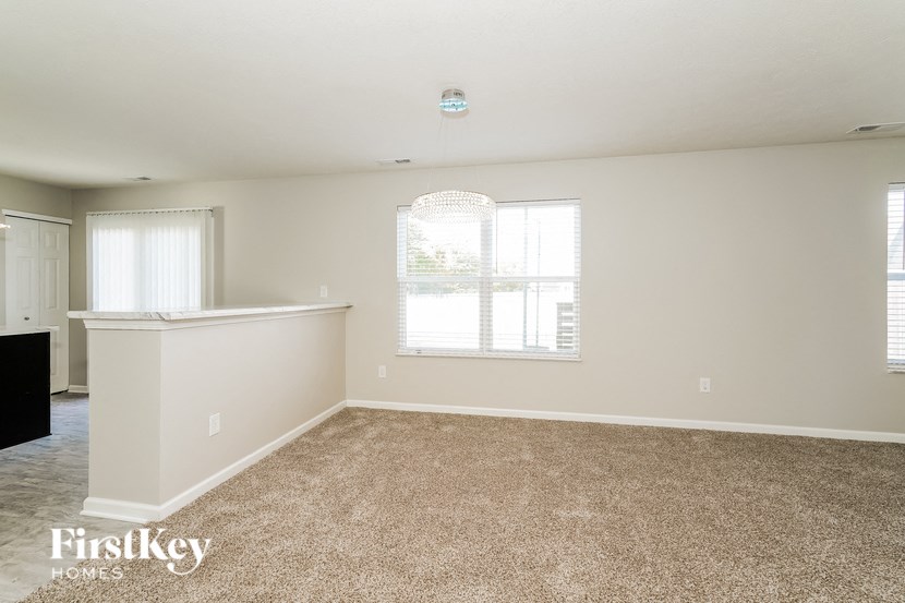 A spacious room with a carpeted floor and a window with blinds.