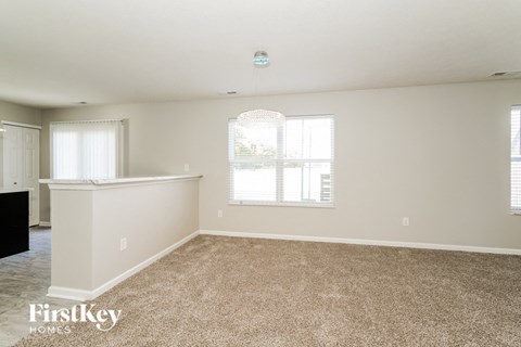A spacious room with a carpeted floor and a window with blinds.