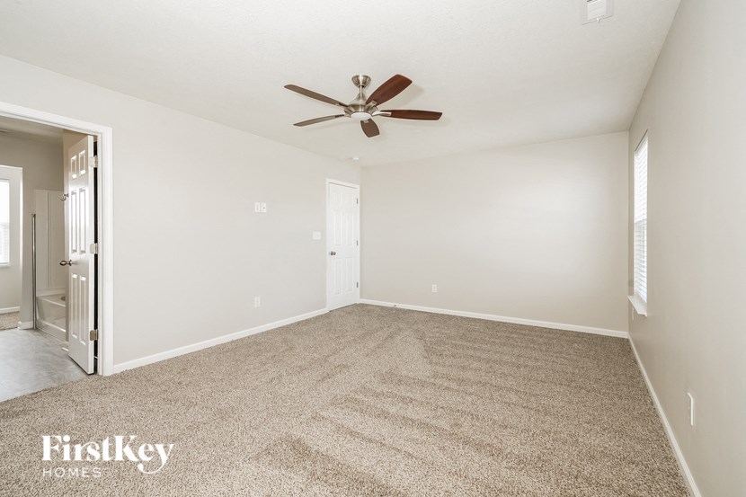 A carpeted room with a ceiling fan and a door.