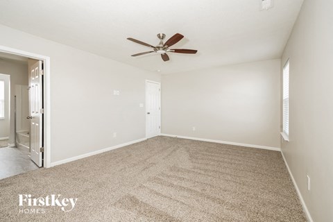 A carpeted room with a ceiling fan and a door.