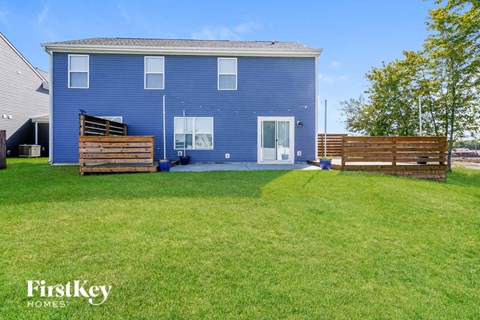 A blue house with a white door and windows is surrounded by a green lawn.