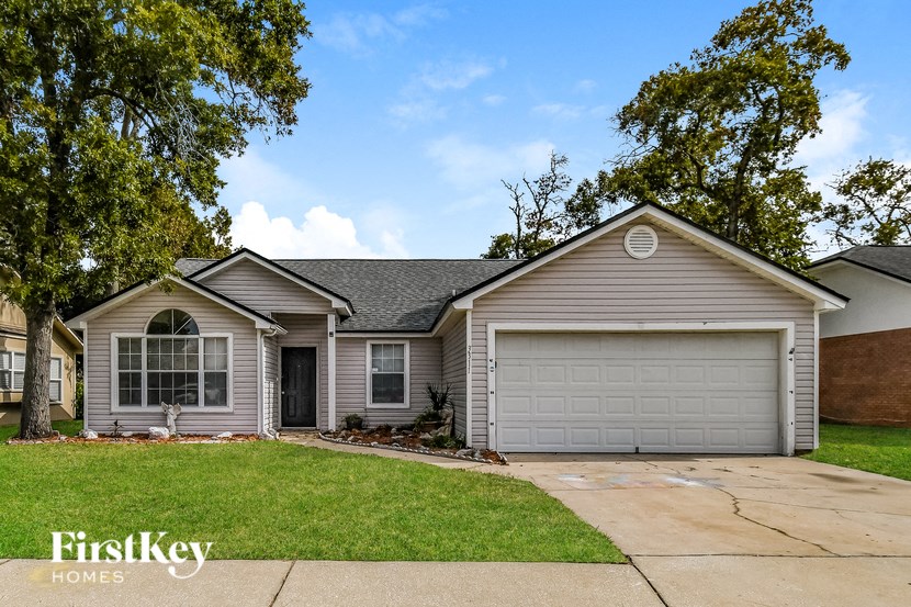 a beige and gray house with a lawn and trees