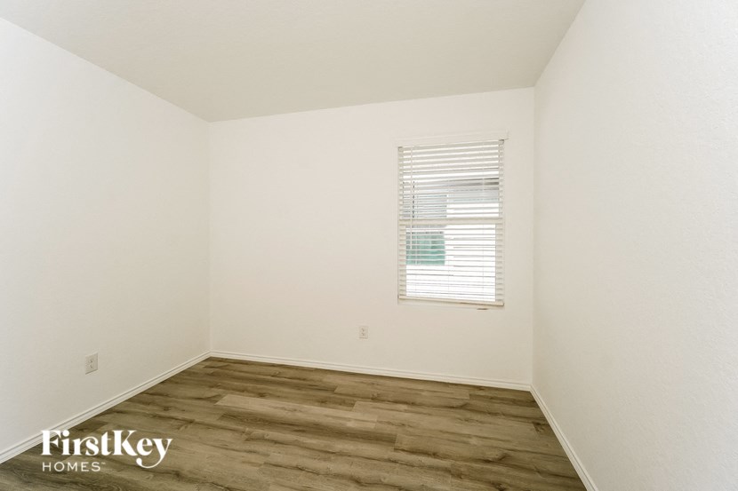 a bedroom with white walls and wood floors and a window